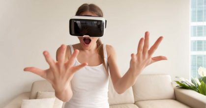 Surprised excited young girl wearing VR glasses looking at hands